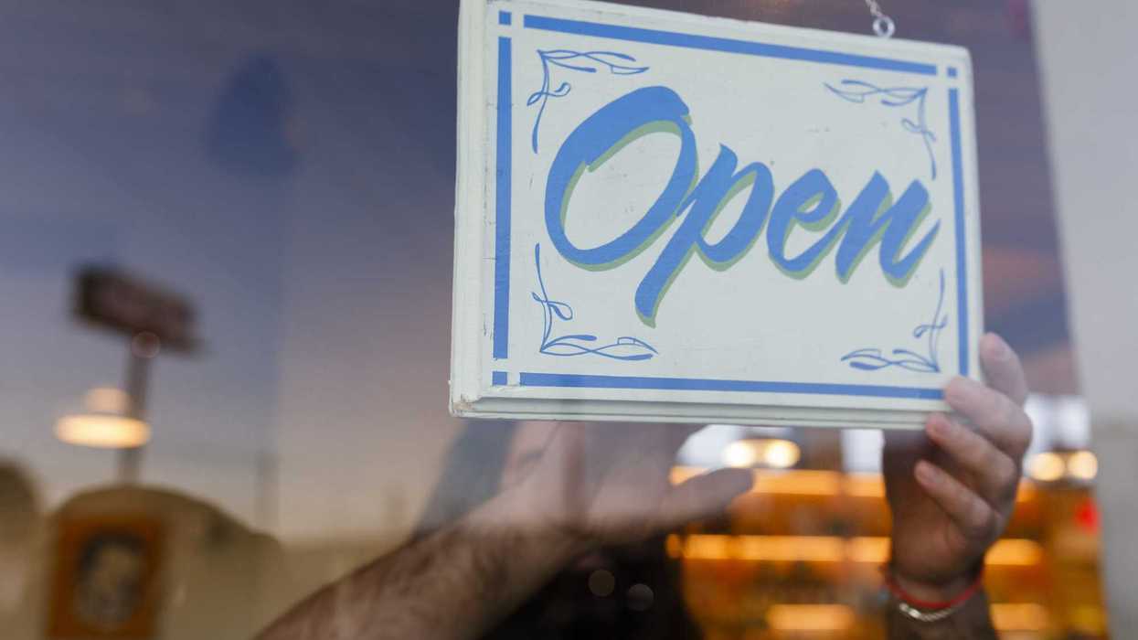 A café owner hangs an “Open” sign on the front door at the start of the business day. Concept of entrepreneurship and readiness.