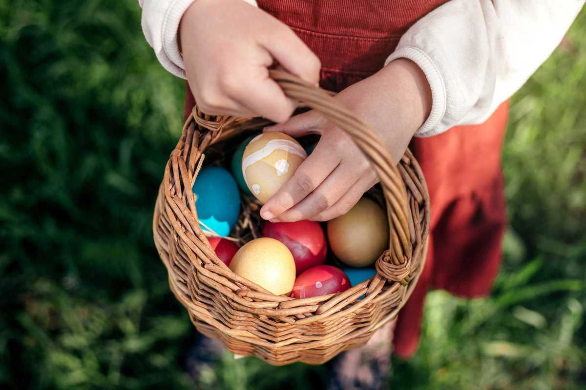 A child holding a basket full of colorfully painted eggs.