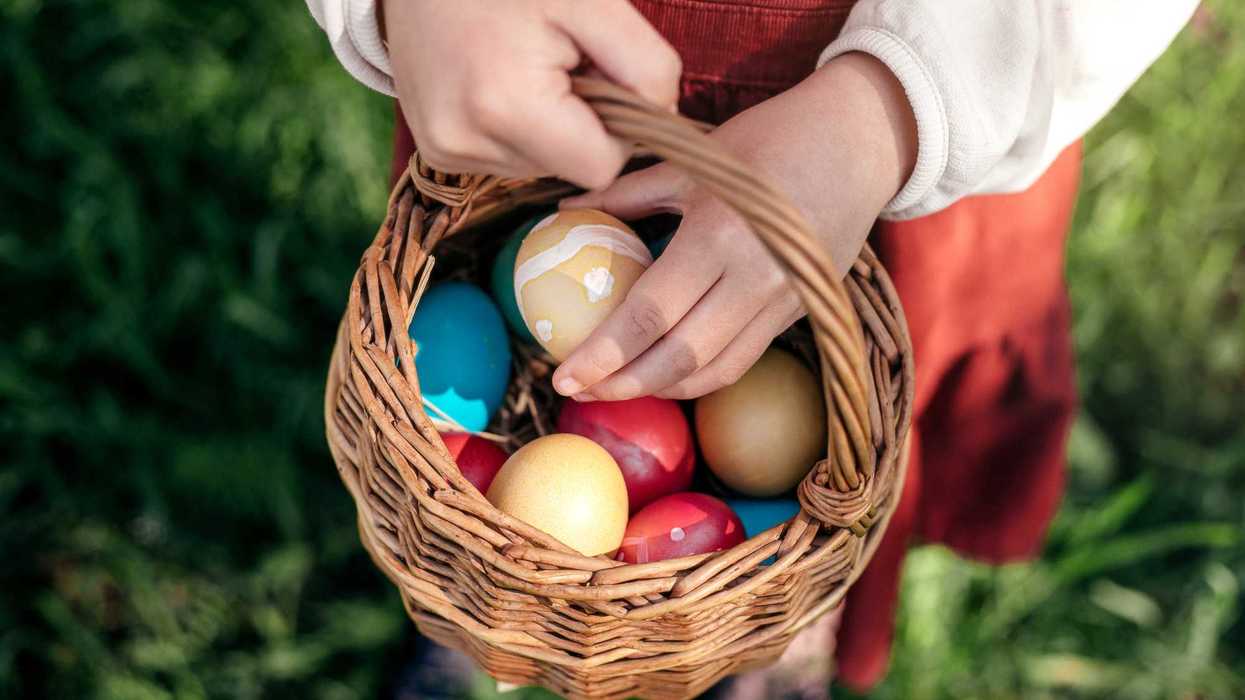 A child holding a basket full of colorfully painted eggs.