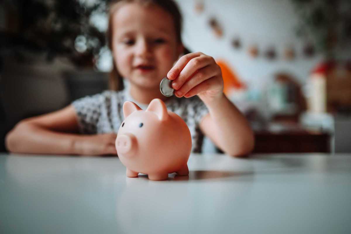 A child putting a coin in a small piggy bank.