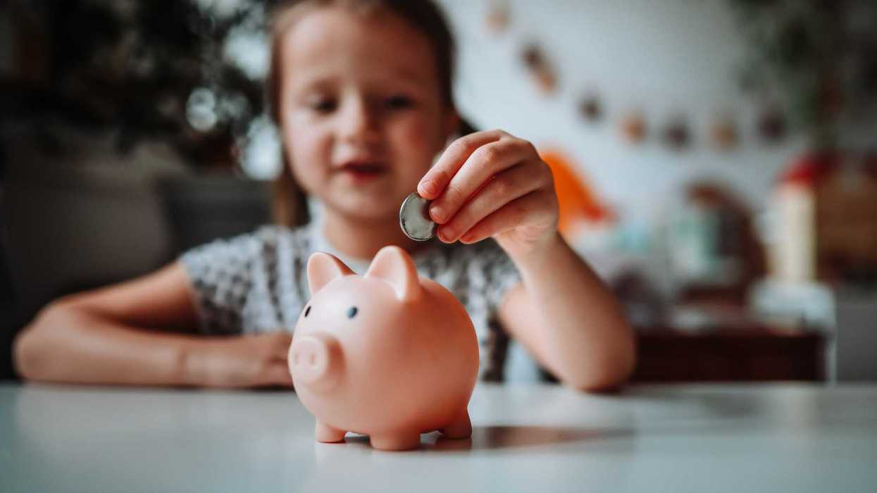 A child putting a coin in a small piggy bank.