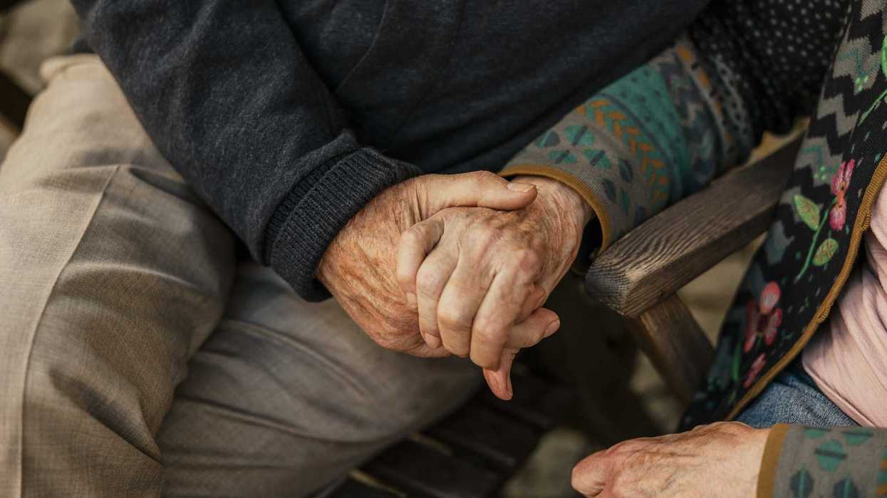 A close up of two elderly individuals holding hands.