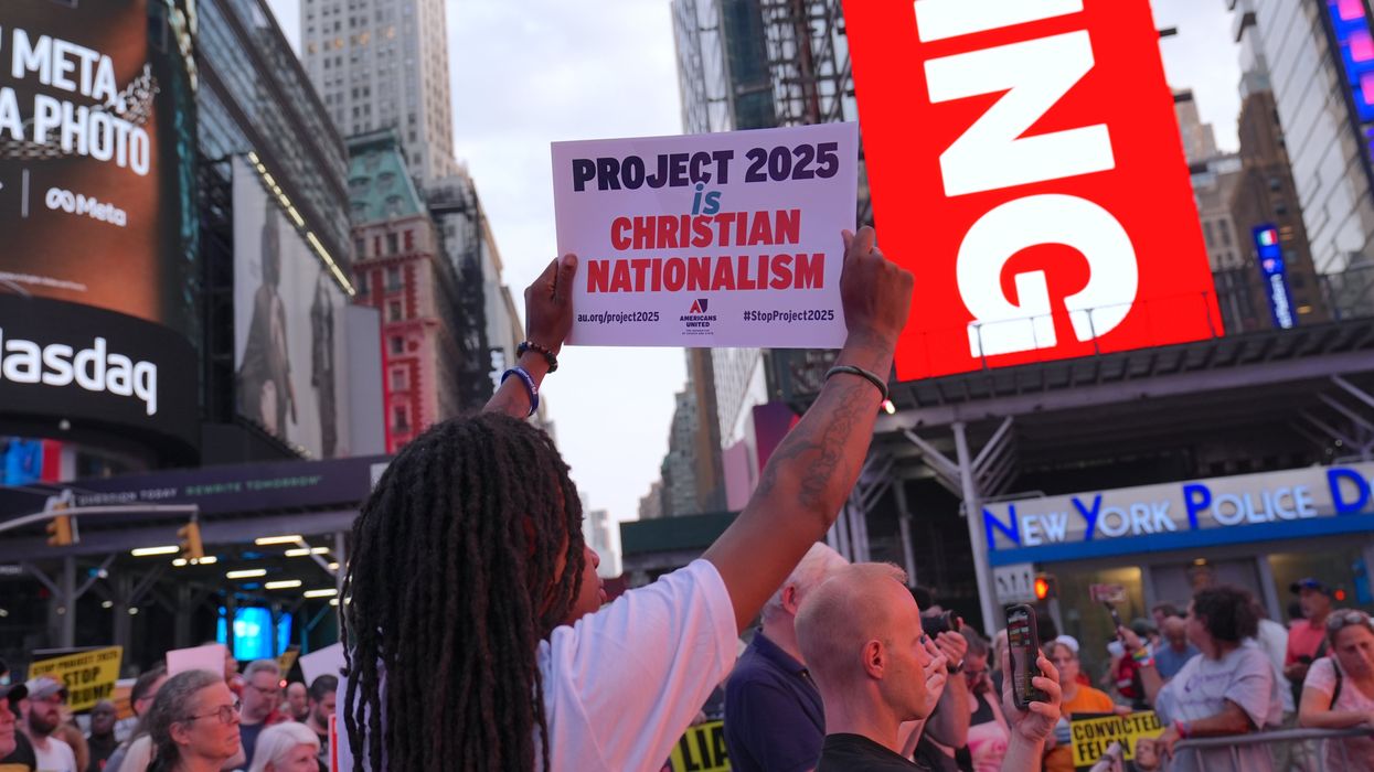 A crowd of protesters in Times Square, New York City, with one person holding a sign that reads "PROJECT 2025 is CHRISTIAN NATIONALISM" by Americans United for Separation of Church and State. The sign includes the hashtags #StopProject2025 and au.org/project2025. The background features prominent advertisements, including a Meta billboard and the Nasdaq building.