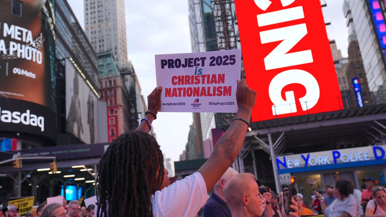 A crowd of protesters in Times Square,, with one person holding a sign that reads "PROJECT 2025 is CHRISTIAN NATIONALISM" by Americans United for Separation of Church and State. The sign includes the hashtags #StopProject2025 and au.org/project2025. The background features prominent advertisements, including a Meta billboard and the Nasdaq building.