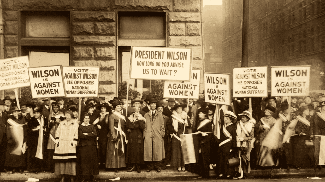 A crowd of protestors standing on a sidewalk, many holding protest signs.