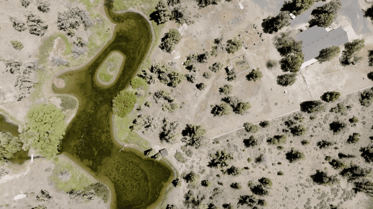 A drone view of dry land with trees around and a lake near the center.