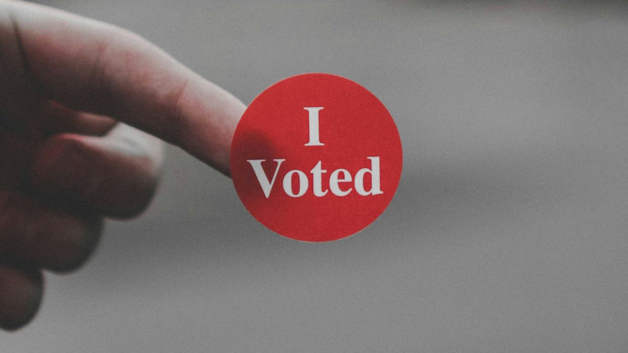 a hand holding a red button that says i vote