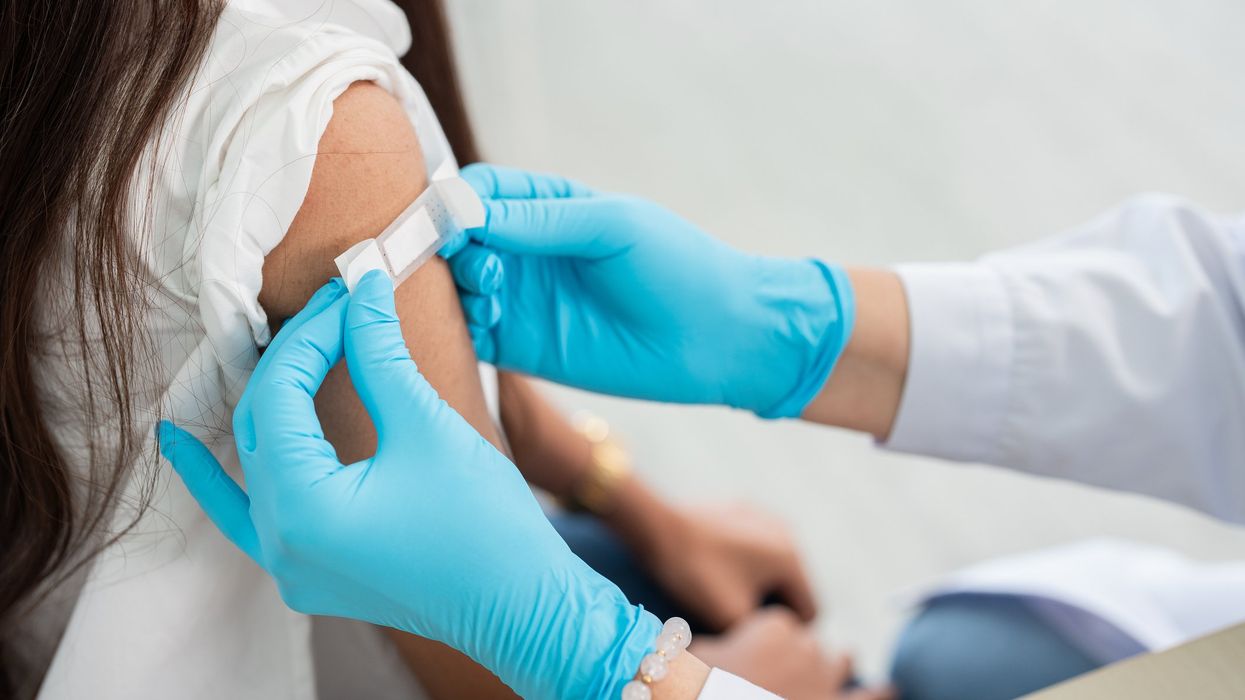 A medical professional wearing gloves, putting a band-aid on a patient's shoulder.