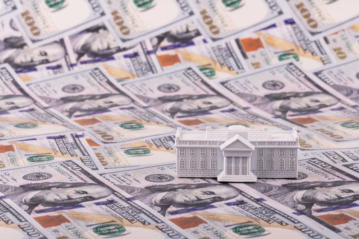 A miniature residence of the President of the United States, the White House, against the backdrop of 100 US dollar bills.
