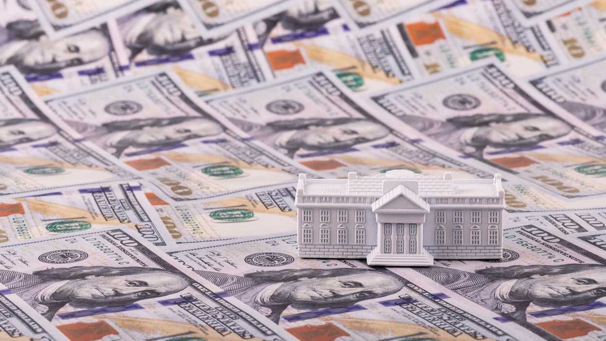 A miniature residence of the President of the United States, the White House, against the backdrop of 100 US dollar bills.