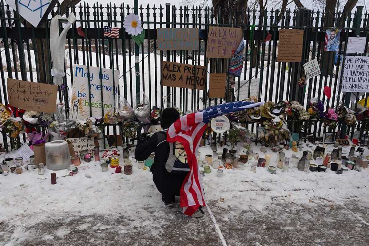 A person holding the U.S. flag, kneeling by a vigil.