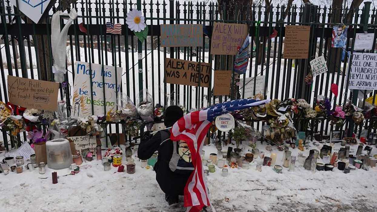A person holding the U.S. flag, kneeling by a vigil.