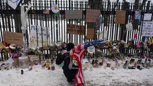 A person holding the U.S. flag, kneeling by a vigil.