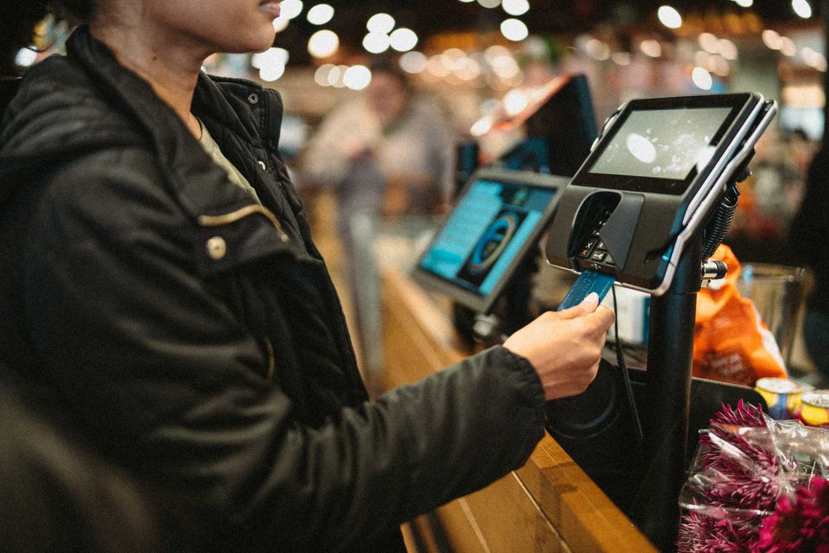 A person in a grocery store, paying with a credit card.