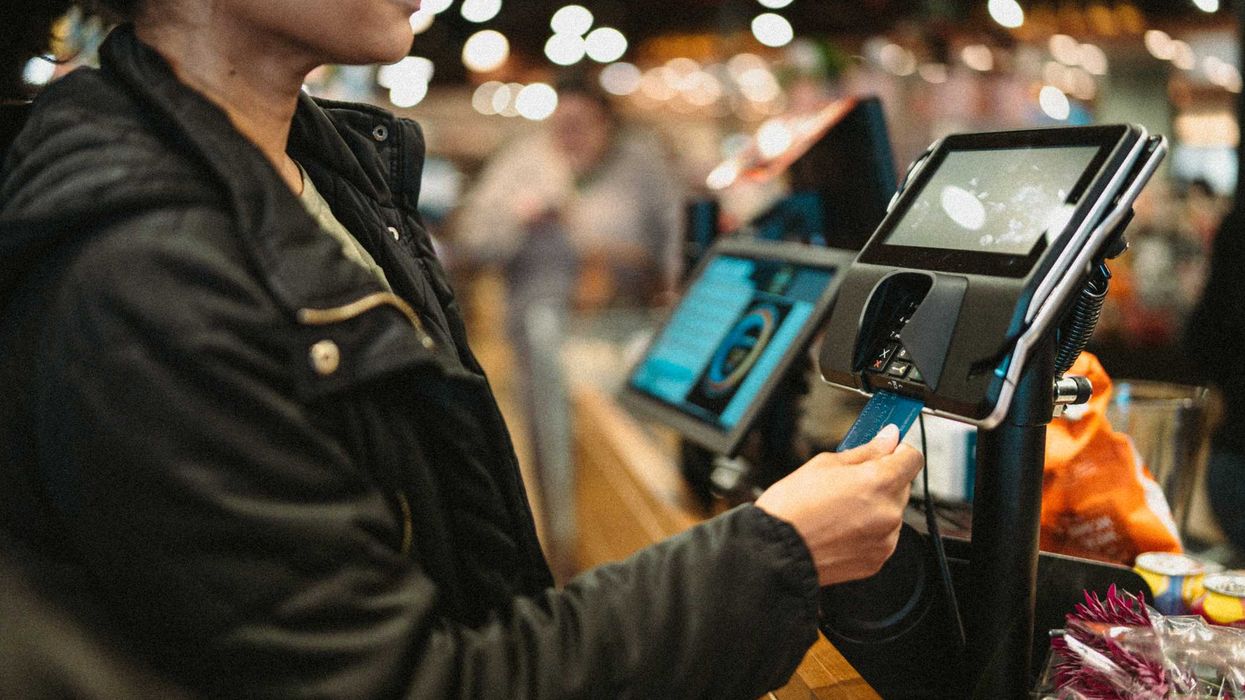 A person in a grocery store, paying with a credit card.