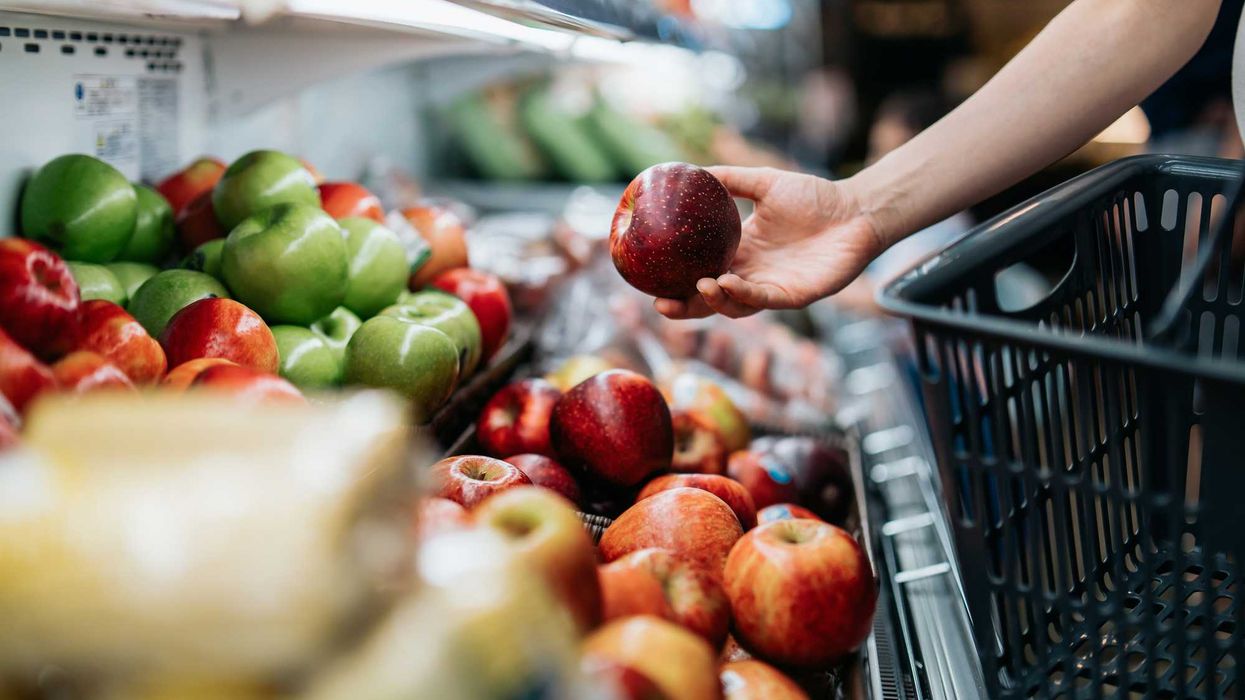 A person in the super market, holding an apple.