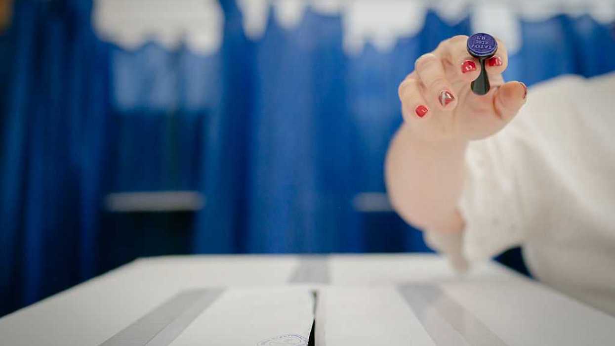 A person's hand holding a stamp above a vote deposit box.