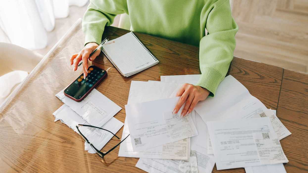 A person sits at a table, going through papers, using a calculator.