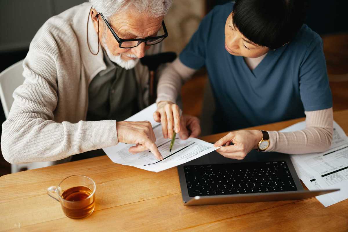 A Senior Man Using A Laptop Computer And Paying Bills With Nurse