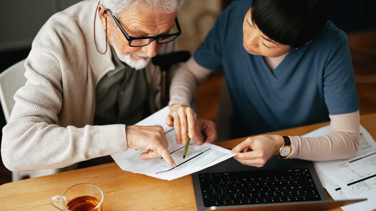 A Senior Man Using A Laptop Computer And Paying Bills With Nurse