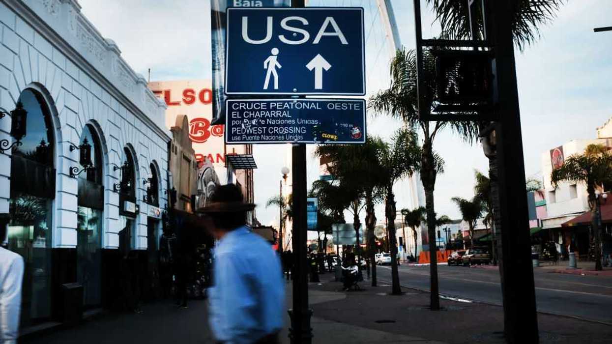 A sign directs pedestrians towards the United States in Tijuana, Mexico. A person walks in the foreground.