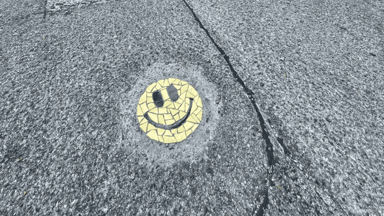 A small colorful smiley-face mosaic patching a pothole.