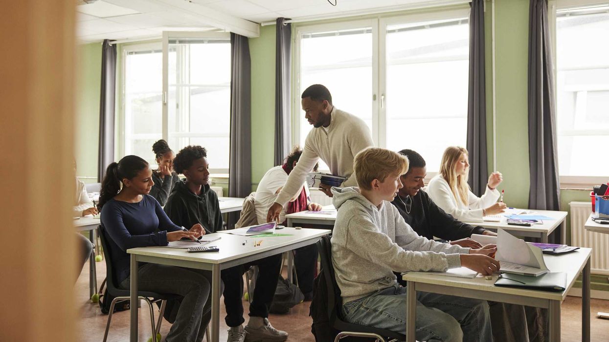 A teacher passing out papers to students in a classroom.
