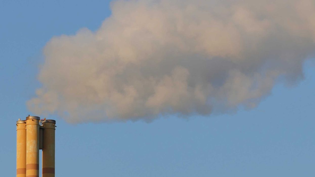 A thick cloud of exhaust rises up from a chimney in the blue sky