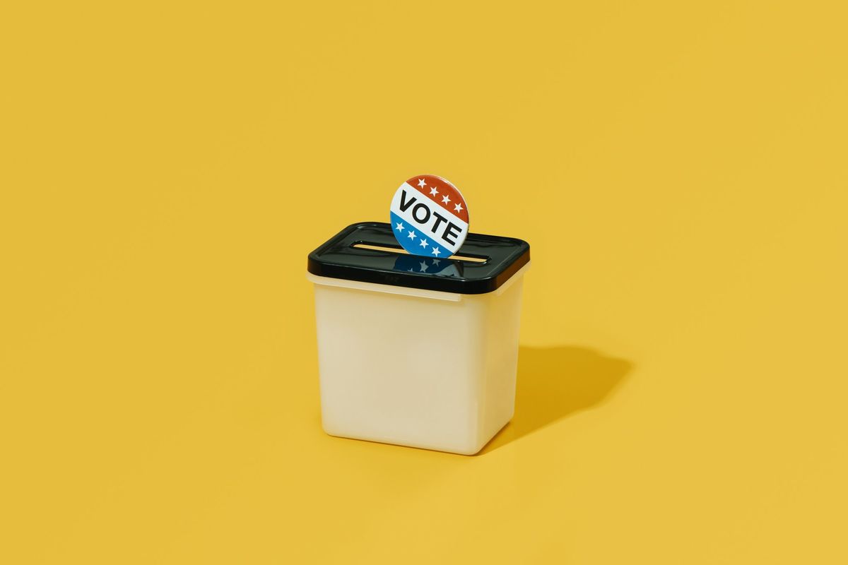 A "vote" sticker or pin going into a ballot box.