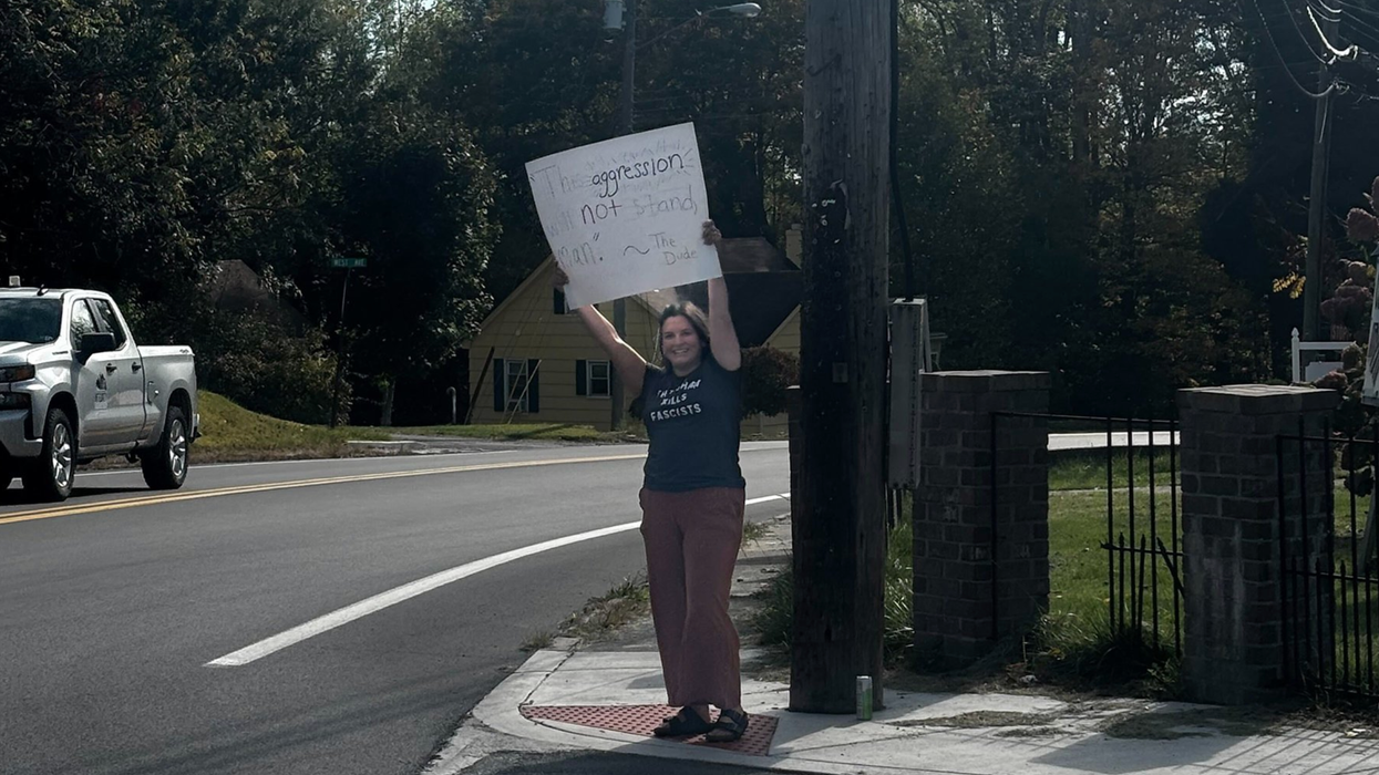 A woman holding up a protest sign at the corner of a sidewalk.