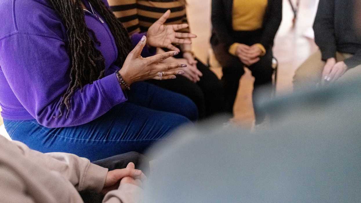A woman sitting down and speaking with a group of people.