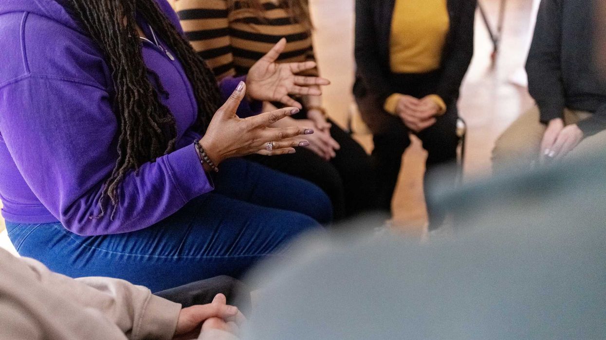 A woman sitting down and speaking with a group of people.