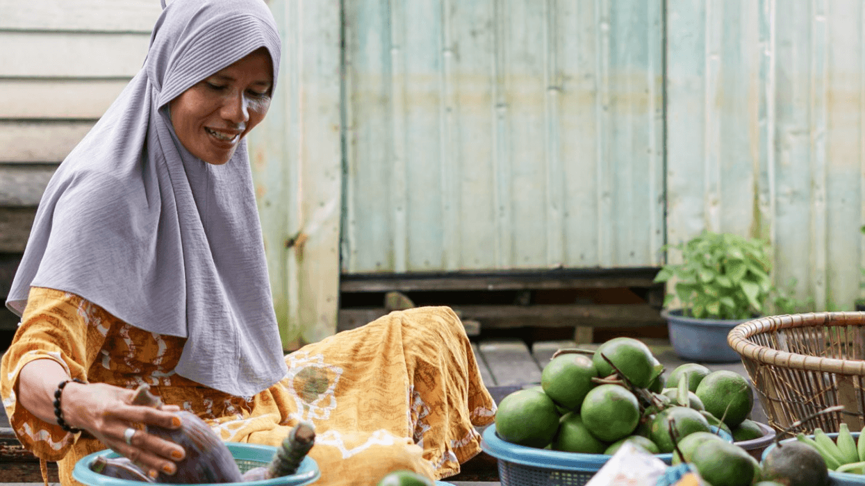 A woman sitting on the ground, with by fruits in baskets around her.