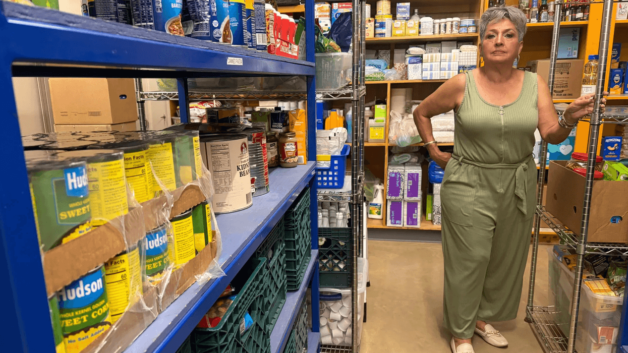 A woman standing in the middle of a food pantry filled with canned and boxed goods and toiletries.