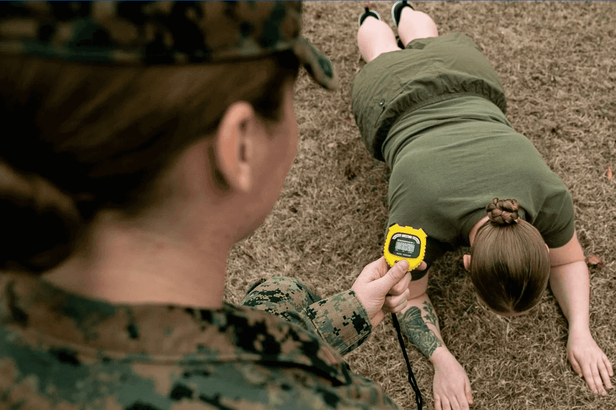 A woman timing another women in the military as she does push ups.