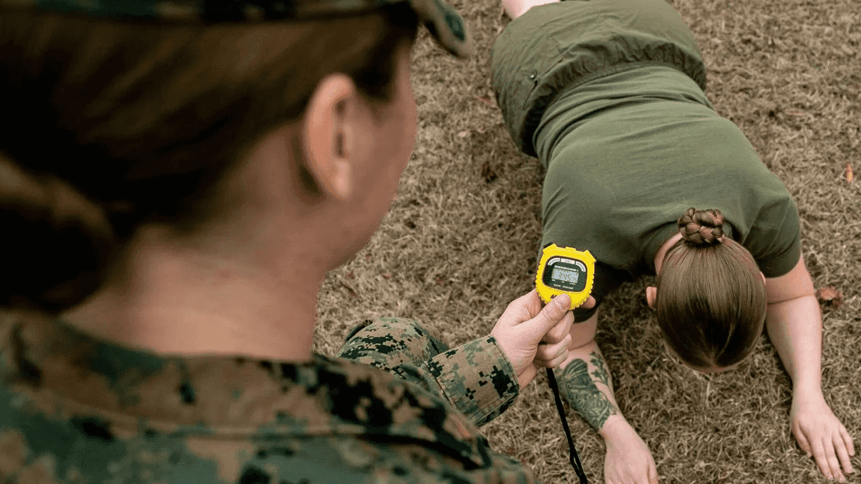 A woman timing another women in the military as she does push ups.