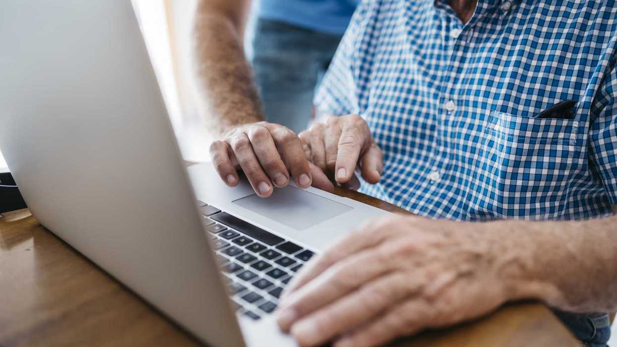 Adult grandson teaching his grandfather to use laptop, close-up.