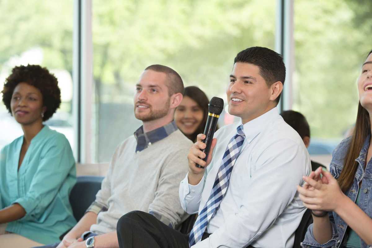 Adult man holds a microphone while asking a question during a town hall meeting.