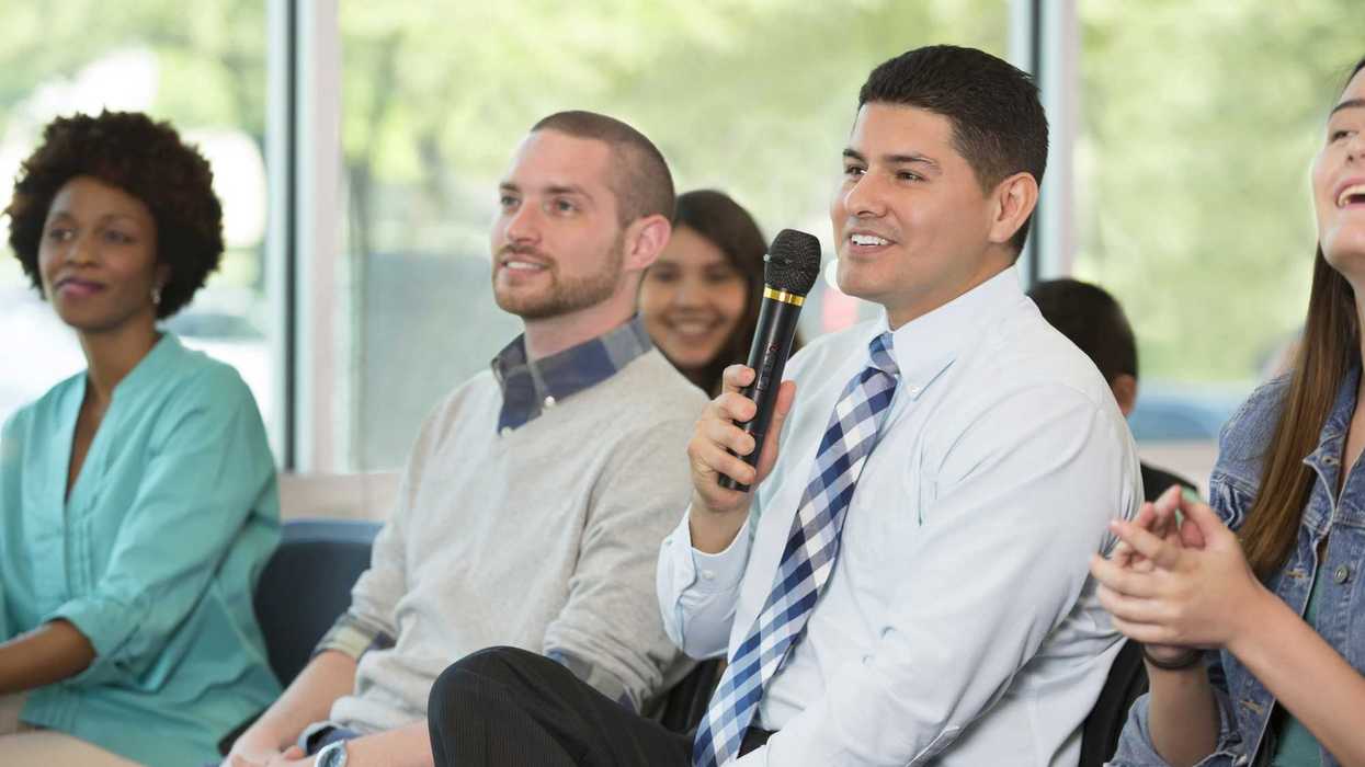 Adult man holds a microphone while asking a question during a town hall meeting.