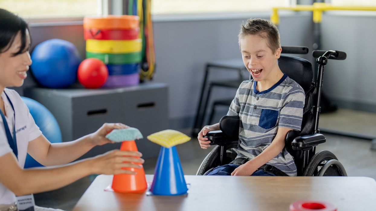 An occupational therapist sits with a young boy at a table as they work on some of his motor skills.