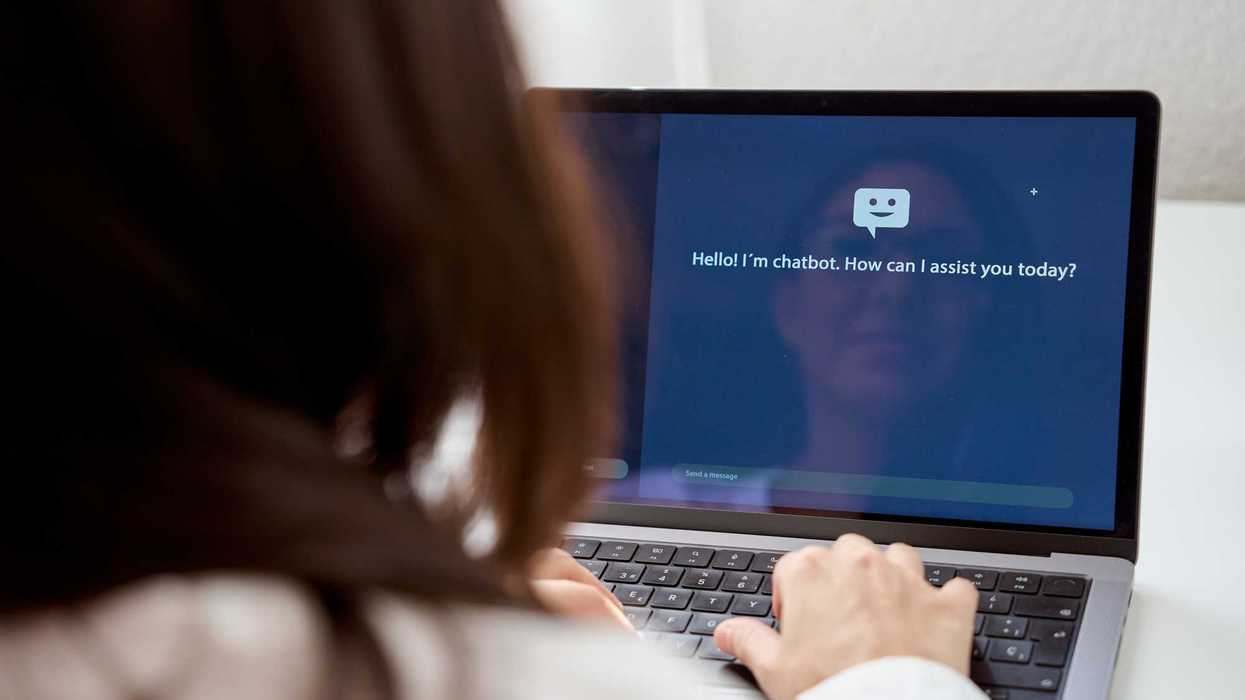 Back view of crop anonymous female talking to a chatbot of computer while sitting at home