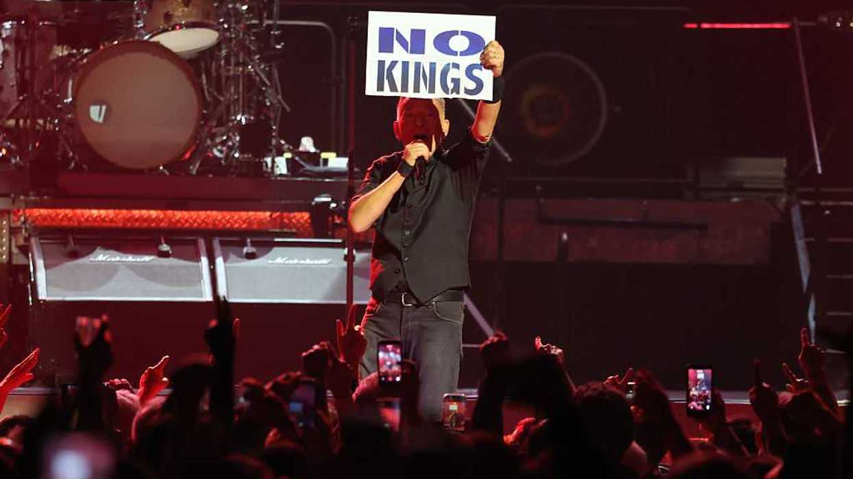 Bruce Springsteen on stage, holding a microphone in one hand and a sign that reads, "No Kings," in the other hand.