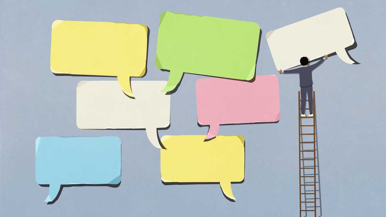 Businessman on ladder arranging large, multicolored speech bubbles on blue background