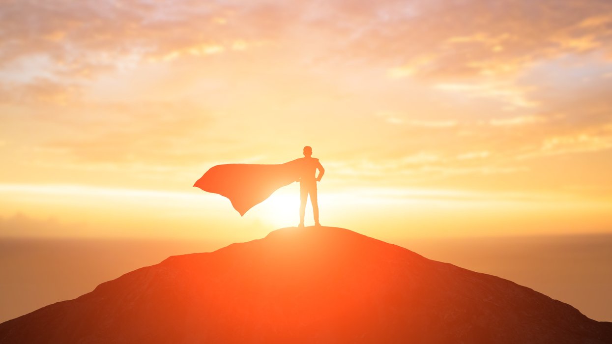Caped person standing on a mountain top