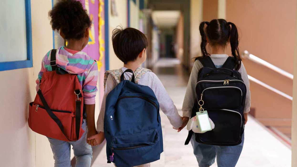 Children holding hands, walking down a school hallway with backpacks on.