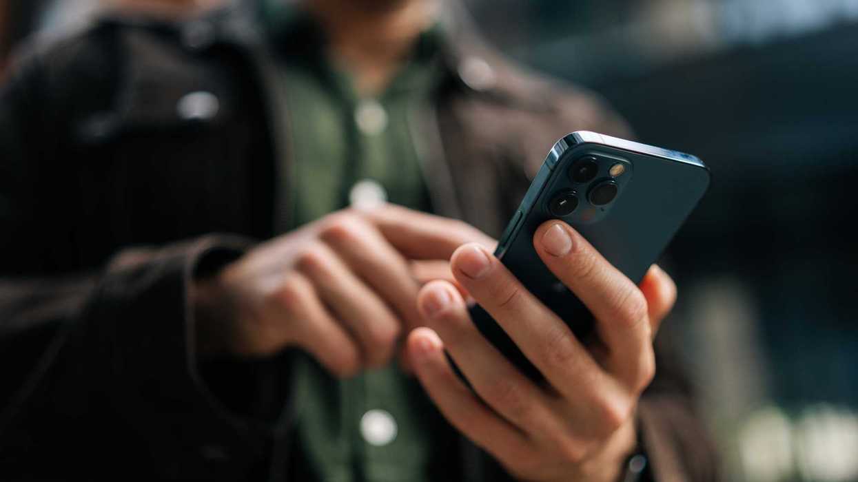 Close-up hands of unrecognizable man holding and using smartphone standing on city street, browsing internet, checking social media, using mobile application.