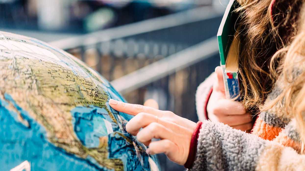 Close-up of a young woman pointing at a globe while holding a book.
