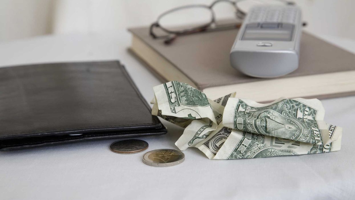 Crumpled dollar bills, two coins, a wallet, book, glasses, and home phone on a table.