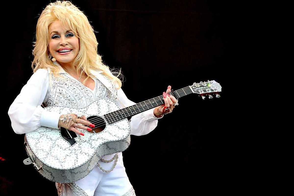 Dolly Parton performs on stage, holding a white, bedazzled guitar.