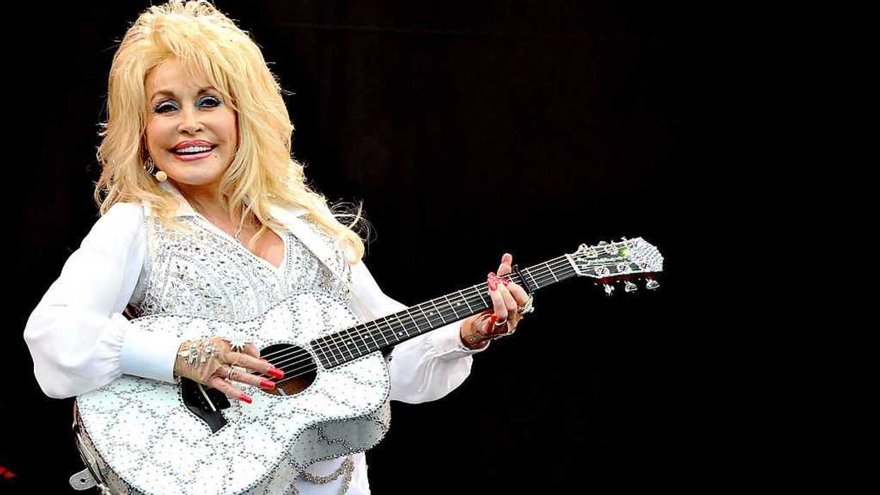 Dolly Parton performs on stage, holding a white, bedazzled guitar.